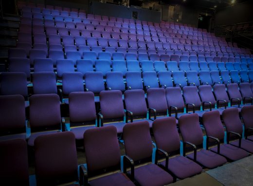 Tyhjä katsomo, joka on valaistu sinisellä teatterivalonheittimellä