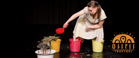 Valkoiseen mekkoon pukeutunut nainen polvistuu lavalla ja kaataa lehtiä punaisesta kauhasta värikkäisiin ämpäreihin. Osiris Teatterin logo näkyy oikeassa alakulmassa.