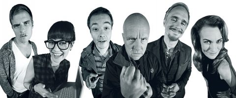 Kuusi ihmistä seisoo peräkkäin kameraan päin liioitelluin ilmein ja asennoin, ja heidät on kuvattu kalansilmälinssillä humoristisen, vääristyneen vaikutelman aikaansaamiseksi.