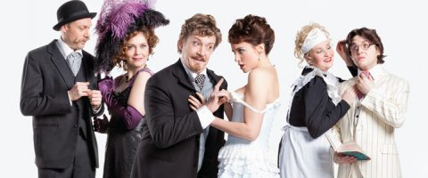Viisi vintage-asuihin pukeutunutta ihmistä poseeraa dramaattisesti; mies keilahattu ja puku, nainen höyhenpukuinen hattu ja mekko, viiksekäs mies, nainen valkoisessa mekossa, palvelustyttö ja mies silmälaseissa ja raidallinen puku.