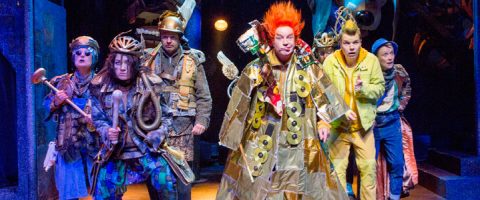 Lavalla seisoo kuusi näyttelijää värikkäissä, omalaatuisissa puvuissa. Heidän asuihinsa kuuluu kypäriä, haarniskoja, kirkkaita peruukkeja ja arkipäiväisistä esineistä valmistettua rekvisiittaa, joka antaa leikkisän, futuristisen tai postapokalyptisen tunnelman. He vaikuttavat ilmeikkäiltä ja eloisilta.