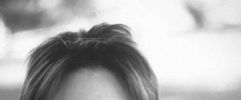 Mustavalkoinen valokuva, jossa näkyy henkilön pään yläosa, jossa on lyhyet, hiukan sekaiset hiukset; silmät ja kasvojen alaosa eivät näy. Tausta on sumea.