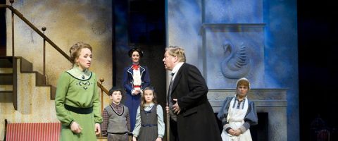 Näyttämöllä nähdään viisi aikuista ja lasta aikakauden puvuissa. Vihreäpukuinen nainen puhuu mustapukuisen miehen kanssa. Kolme lasta ja lastenhoitajaksi pukeutunut nainen seisovat portaikon ja takan, jossa on joutsenreliefi, vieressä.