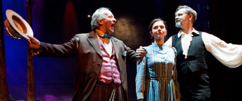 Lavalla esiintyy kolme näyttelijää; ruskeaan pukuun pukeutunut vanhempi mies elehtii dramaattisesti hatullaan, siniseen mekkoon pukeutunut nuori nainen seisoo keskellä, ja toinen liiviin pukeutunut mies seisoo lähellä häntä, kaikki näyttämövalaistuksen alla.