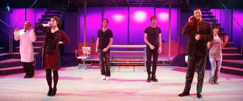 Kuusi näyttelijää esiintyy kirkkaasti valaistulla näyttämöllä, jossa on vaaleanpunainen ja violetti valaistus, seisovat rivissä ja poseeraavat kuin puhelinkeskustelussa. Lavastukseen kuuluu portaita, tuoleja ja lavoja taustalla.