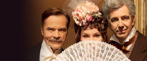 Kolme aikakauden pukuihin pukeutunutta henkilöä, kaksi miestä puvuissa ja kravatissa ja nainen, jolla on kukkapäähine, joka kurkistaa pitsiviuhkan yli, seisovat tiiviisti yhdessä ruskeaa taustaa vasten, mikä tuo mieleen historiallisen miljöön.