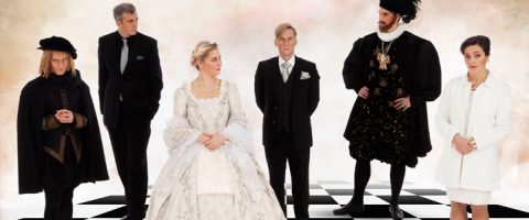 Kuusi historiallisiin ja moderneihin juhlavaatteisiin pukeutunutta henkilöä seisoo mustavalkoisella shakkilaudalla kasvot eteenpäin. Heidän asentonsa ja pukeutumisensa tuovat mieleen shakkipelin teeman.