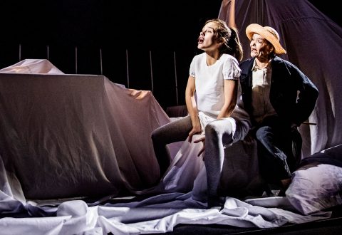 Kaksi näyttelijää esiintyy näyttämöllä valkoisen verhotun kankaan ympäröimänä. Toinen, vaaleisiin vaatteisiin pukeutunut, istuu polvet koukussa ja katsoo ilmeikkäästi ylöspäin; toinen, tummiin vaatteisiin ja olkihattuun pukeutunut, seisoo takana ja katsoo samaan suuntaan.