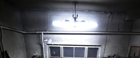 Hämärästi valaistu, likainen huone, jonka seinät ovat halkeilleet, putket ovat paljaina, katossa on loisteputkivalaisin ja valon alla on likainen ikkuna.