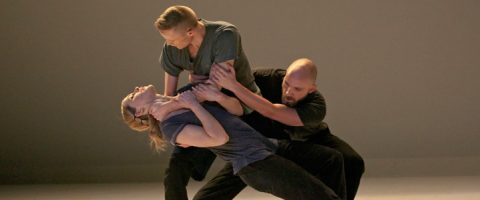 Lavalla esiintyy kolme tanssijaa; kaksi miestä tukee naista, joka nojaa dramaattisesti taaksepäin, kehon kieli on ilmeikäs ja keskittyy intensiivisesti, ja kaikki ovat pukeutuneet rentoihin tummiin vaatteisiin neutraalia taustaa vasten.