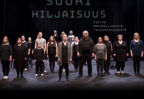 Monipuolinen joukko ihmisiä seisoo kasvot menosuuntaan pimeällä näyttämöllä suomenkielisten sanojen Suuri Hiljaisuus alla. Heidän takanaan on tuoleja ja oikealla puolella teksti: Esitys mahdollisesta tulevaisuudesta.