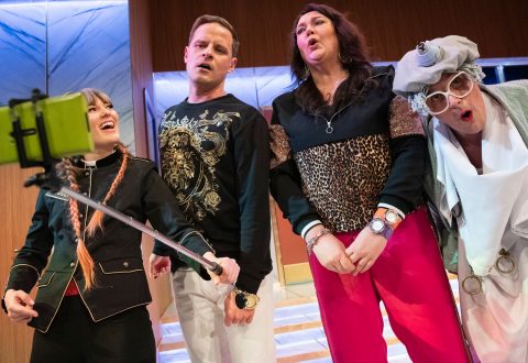 Neljä ihmistä poseeraa yhdessä ja tekee ilmeikkäitä ilmeitä selfie-kuvaan selfie-tikkuun kiinnitetyllä älypuhelimella. Heidän asunsa ovat eklektisiä ja huomiota herättäviä, ja rohkeat kuviot ja asusteet luovat eloisan ja teatraalisen ilmapiirin.