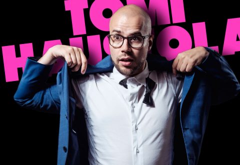 Silmälasipäinen ja kalju mies säätää sinistä puvuntakkinsa ja paljastaa solmimattoman mustan rusetin. Taustalla on suuri vaaleanpunainen teksti TOMI HAUSOLA.