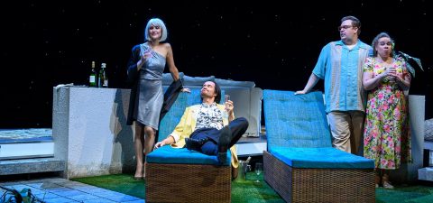 Neljä ihmistä on modernilla terassilla tähtivalojen alla. Yksi hopeamekkoon pukeutunut nainen seisoo viinipullojen ääressä, keltaiseen takkiin pukeutunut mies loikoilee tuolilla, kun taas toinen mies ja kukkamekkoon pukeutunut nainen seisovat yhdessä yllättyneen näköisinä.