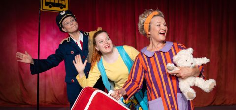 Lavalla esiintyy kolme värikkäisiin asuihin pukeutunutta aikuista; yhdellä on poliisin univormu, toisella kirkkaan keltainen ja letit, ja kolmas pitää hymyillen nallea kädessään ja pukeutuu pyjamaan. Taustalla on bussipysäkin merkki.