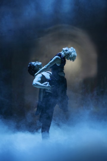 Kaksi balettitanssijaa esiintyy dramaattisesti sumuisessa, sinisellä valaistussa maisemassa. Toinen tanssija nostaa ja tukee toista tanssijaa, joka nojaa taaksepäin viehkeästi kädet ojennettuina, luoden ilmeikkään ja teatraalisen hetken.