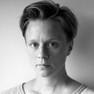 Mustavalkoinen muotokuva lyhythiuksisesta henkilöstä, jolla on vaalea toppi ja joka katsoo suoraan kameraan neutraali ilme kasvoillaan tavallista taustaa vasten.