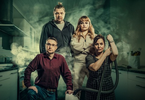 Neljä aikuista poseeraa savuisessa keittiössä. Yhdellä edessä olevalla miehellä on silmälasit ja punainen paita, ja hän polvistuu, kun taas toinen seisoo hänen takanaan tummassa hupparissa. Kaksi naista seisoo oikealla, toinen vaaleissa vaatteissa, toinen esiliina kädessään imuriletku.