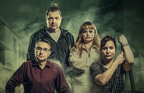 Neljä henkilöä seisoo yhdessä dramaattisessa valaistuksessa ja savussa. Edessä on kaksi naista, joista toinen pitää kädessään imurin letkua, ja heidän takanaan seisoo kaksi miestä; kaikki katsovat vakavasti kameraan.
